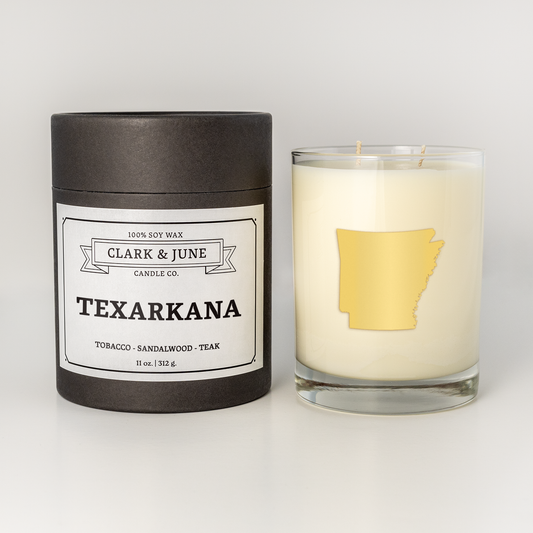 Double wicked soy candle in a 13.5 oz tumbler with the state of  Arkansas printed in 22k gold foil on the face. Black cylinder packaging with Texarkana on the label. SEO Text – Drinking glass, soy wax candle, Christmas Candle, hand poured, small batch, scented candle, Woman Owned, local candle, Housewarming present, gives back, charity, community candle, becomes a cocktail glass, closing gift.