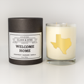 Load image into Gallery viewer, Double wicked soy candle in a 13.5 oz tumbler with the state of Texas printed in 22k gold foil on the face. Black cylinder packaging with “Welcome Home” on the label. SEO Text – Drinking glass, soy wax candle, Texas candle, hand poured, small batch, scented candle, Woman Owned, local candle, Housewarming present, gives back, charity, community candle, becomes a cocktail glass, closing gift.