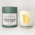 Load image into Gallery viewer, Double wicked soy candle in a 13.5 oz tumbler with the state of   Georgia printed in 22k gold foil on the face. Green cylinder packaging with Christmas in "Your Town" on the label. SEO Text – Drinking glass, soy wax candle, Christmas Candle, hand poured, small batch, scented candle, Woman Owned, local candle, Housewarming present, gives back, charity, community candle, becomes a cocktail glass, closing gift.