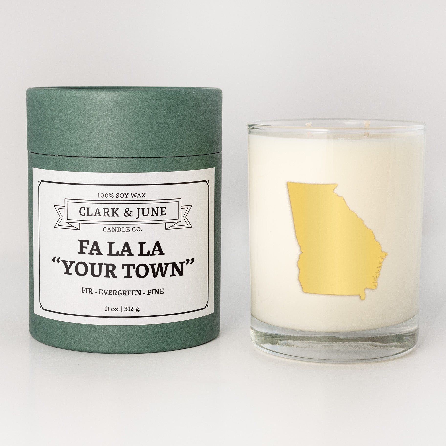 Double wicked soy candle in a 13.5 oz tumbler with the state of   Georgia printed in 22k gold foil on the face. Green cylinder packaging with Fa La La "Your Town" on the label. SEO Text – Drinking glass, soy wax candle, Christmas Candle, hand poured, small batch, scented candle, Woman Owned, local candle, Housewarming present, gives back, charity, community candle, becomes a cocktail glass, closing gift.