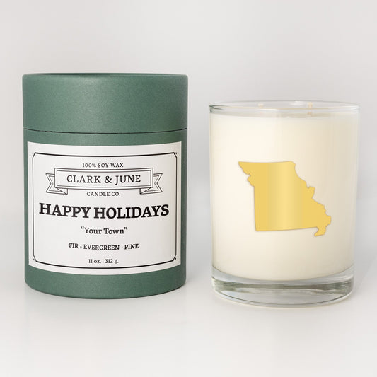 Double wicked soy candle in a 13.5 oz tumbler with the state of   Missouri printed in 22k gold foil on the face. Green cylinder packaging with Happy Holidays in "Your Town" on the label. SEO Text – Drinking glass, soy wax candle, Christmas Candle, hand poured, small batch, scented candle, Woman Owned, local candle, Housewarming present, gives back, charity, community candle, becomes a cocktail glass, closing gift.
