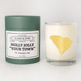 Load image into Gallery viewer, Double wicked soy candle in a 13.5 oz tumbler with the state of   South Carolina printed in 22k gold foil on the face. Green cylinder packaging with Holly Jolly "Your Town" on the label. SEO Text – Drinking glass, soy wax candle, Christmas Candle, hand poured, small batch, scented candle, Woman Owned, local candle, Housewarming present, gives back, charity, community candle, becomes a cocktail glass, closing gift.