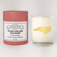 Load image into Gallery viewer, Double wicked soy candle in a 13.5 oz tumbler with the state of  North Carolina printed in 22k gold foil on the face. Red cylinder packaging with Home for the Holidays  North Carolina on the label. SEO Text – Drinking glass, soy wax candle, Christmas Candle, hand poured, small batch, scented candle, Woman Owned, local candle, Housewarming present, gives back, charity, community candle, becomes a cocktail glass, closing gift.
