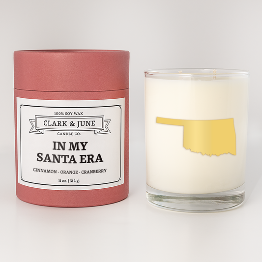 Double wicked soy candle in a 13.5 oz tumbler with the state of  Oklahoma printed in 22k gold foil on the face. Red cylinder packaging with In my Santa Era on the label. SEO Text – Drinking glass, soy wax candle, Christmas Candle, hand poured, small batch, scented candle, Woman Owned, local candle, Housewarming present, gives back, charity, community candle, becomes a cocktail glass, closing gift.