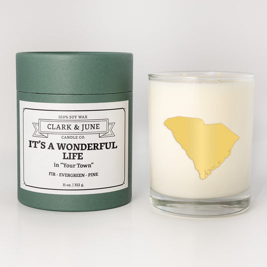Double wicked soy candle in a 13.5 oz tumbler with the state of South Carolinaprinted in 22k gold foil on the face. Green cylinder packaging with It's a Wonderful Life in "Your Town"on the label. SEO Text – Drinking glass, soy wax candle, Christmas Candle, hand poured, small batch, scented candle, Woman Owned, local candle, Housewarming present, gives back, charity, community candle, becomes a cocktail glass, closing gift.