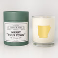 Load image into Gallery viewer, Double wicked soy candle in a 13.5 oz tumbler with the state of   Arkansas printed in 22k gold foil on the face. Green cylinder packaging with Merry "Your Town" on the label. SEO Text – Drinking glass, soy wax candle, Christmas Candle, hand poured, small batch, scented candle, Woman Owned, local candle, Housewarming present, gives back, charity, community candle, becomes a cocktail glass, closing gift.