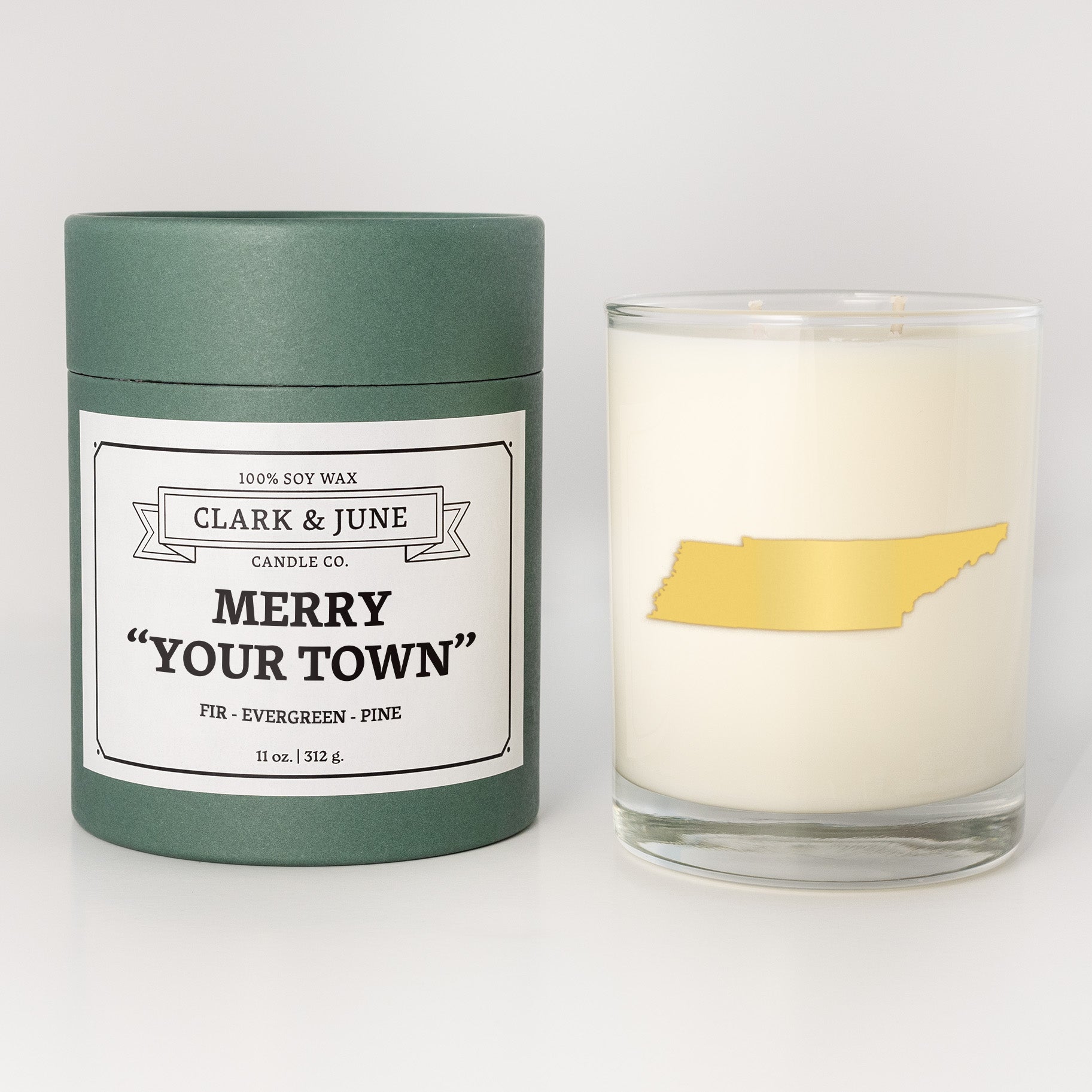 Double wicked soy candle in a 13.5 oz tumbler with the state of   Tennessee printed in 22k gold foil on the face. Green cylinder packaging with Merry "Your Town" on the label. SEO Text – Drinking glass, soy wax candle, Christmas Candle, hand poured, small batch, scented candle, Woman Owned, local candle, Housewarming present, gives back, charity, community candle, becomes a cocktail glass, closing gift.