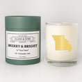 Load image into Gallery viewer, Double wicked soy candle in a 13.5 oz tumbler with the state of Missouriprinted in 22k gold foil on the face. Green cylinder packaging with Merry & Bright in "Your Town"on the label. SEO Text – Drinking glass, soy wax candle, Christmas Candle, hand poured, small batch, scented candle, Woman Owned, local candle, Housewarming present, gives back, charity, community candle, becomes a cocktail glass, closing gift.