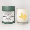 Load image into Gallery viewer, Double wicked soy candle in a 13.5 oz tumbler with the state of   Texas printed in 22k gold foil on the face. Green cylinder packaging with Merry & Bright in "Your Town" on the label. SEO Text – Drinking glass, soy wax candle, Christmas Candle, hand poured, small batch, scented candle, Woman Owned, local candle, Housewarming present, gives back, charity, community candle, becomes a cocktail glass, closing gift.