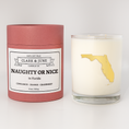 Load image into Gallery viewer, Double wicked soy candle in a 13.5 oz tumbler with the state of  Florida printed in 22k gold foil on the face. Red cylinder packaging with Naughty or Nice on the label. SEO Text – Drinking glass, soy wax candle, Christmas Candle, hand poured, small batch, scented candle, Woman Owned, local candle, Housewarming present, gives back, charity, community candle, becomes a cocktail glass, closing gift.