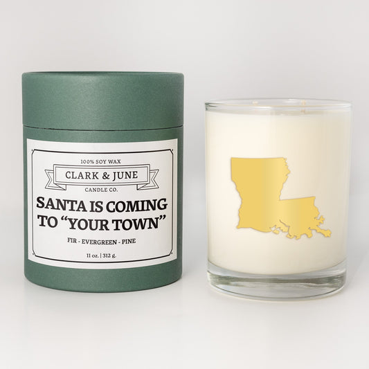 Double wicked soy candle in a 13.5 oz tumbler with the state of   Louisiana printed in 22k gold foil on the face. Green cylinder packaging with Santa is Coming to "Your Town" on the label. SEO Text – Drinking glass, soy wax candle, Christmas Candle, hand poured, small batch, scented candle, Woman Owned, local candle, Housewarming present, gives back, charity, community candle, becomes a cocktail glass, closing gift.