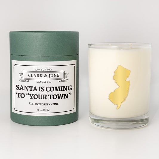 Double wicked soy candle in a 13.5 oz tumbler with the state of New Jerseyprinted in 22k gold foil on the face. Green cylinder packaging with Santa is Coming to "Your Town"on the label. SEO Text – Drinking glass, soy wax candle, Christmas Candle, hand poured, small batch, scented candle, Woman Owned, local candle, Housewarming present, gives back, charity, community candle, becomes a cocktail glass, closing gift.