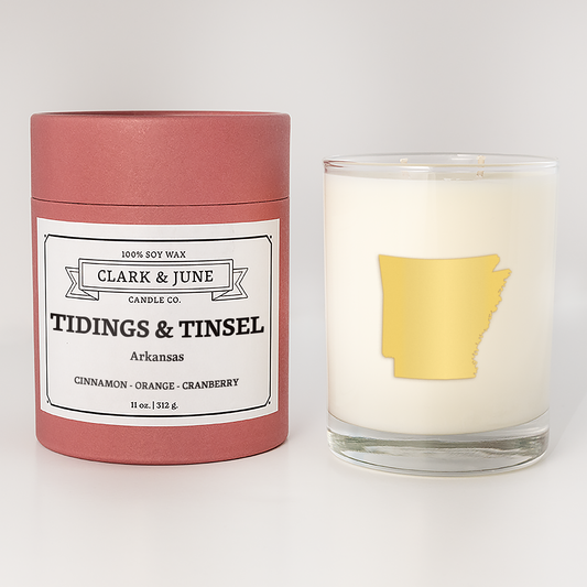 Double wicked soy candle in a 13.5 oz tumbler with the state of  Arkansas printed in 22k gold foil on the face. Red cylinder packaging with Tidings & Tinsel Arkansas on the label. SEO Text – Drinking glass, soy wax candle, Christmas Candle, hand poured, small batch, scented candle, Woman Owned, local candle, Housewarming present, gives back, charity, community candle, becomes a cocktail glass, closing gift.