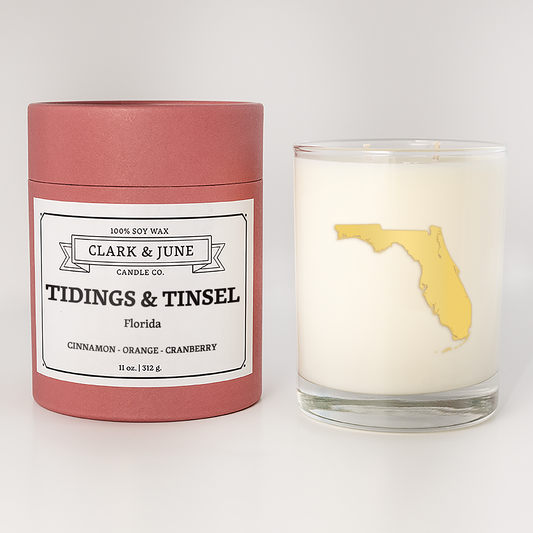 Double wicked soy candle in a 13.5 oz tumbler with the state of  Florida printed in 22k gold foil on the face. Red cylinder packaging with Tidings & Tinsel Florida on the label. SEO Text – Drinking glass, soy wax candle, Christmas Candle, hand poured, small batch, scented candle, Woman Owned, local candle, Housewarming present, gives back, charity, community candle, becomes a cocktail glass, closing gift.
