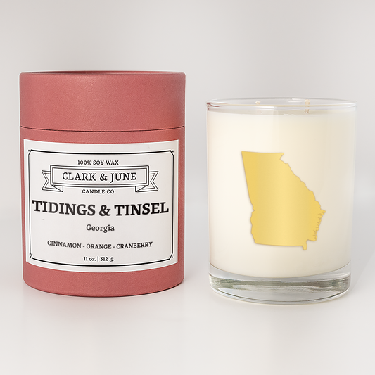 Double wicked soy candle in a 13.5 oz tumbler with the state of  Georgia printed in 22k gold foil on the face. Red cylinder packaging with Tidings & Tinsel Georgia on the label. SEO Text – Drinking glass, soy wax candle, Christmas Candle, hand poured, small batch, scented candle, Woman Owned, local candle, Housewarming present, gives back, charity, community candle, becomes a cocktail glass, closing gift.