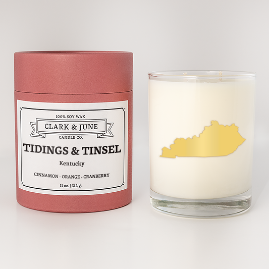Double wicked soy candle in a 13.5 oz tumbler with the state of  Kentucky printed in 22k gold foil on the face. Red cylinder packaging with Tidings & Tinsel Kentucky on the label. SEO Text – Drinking glass, soy wax candle, Christmas Candle, hand poured, small batch, scented candle, Woman Owned, local candle, Housewarming present, gives back, charity, community candle, becomes a cocktail glass, closing gift.