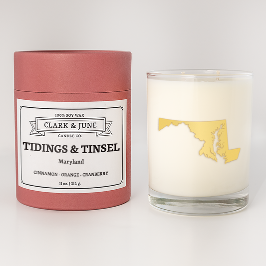 Double wicked soy candle in a 13.5 oz tumbler with the state of  Maryland printed in 22k gold foil on the face. Red cylinder packaging with Tidings & Tinsel Maryland on the label. SEO Text – Drinking glass, soy wax candle, Christmas Candle, hand poured, small batch, scented candle, Woman Owned, local candle, Housewarming present, gives back, charity, community candle, becomes a cocktail glass, closing gift.