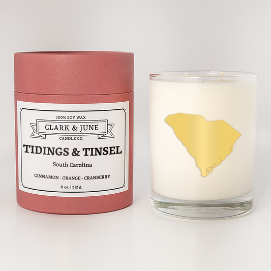 Double wicked soy candle in a 13.5 oz tumbler with the state of  South Carolina printed in 22k gold foil on the face. Red cylinder packaging with Tidings & Tinsel South Carolina on the label. SEO Text – Drinking glass, soy wax candle, Christmas Candle, hand poured, small batch, scented candle, Woman Owned, local candle, Housewarming present, gives back, charity, community candle, becomes a cocktail glass, closing gift.