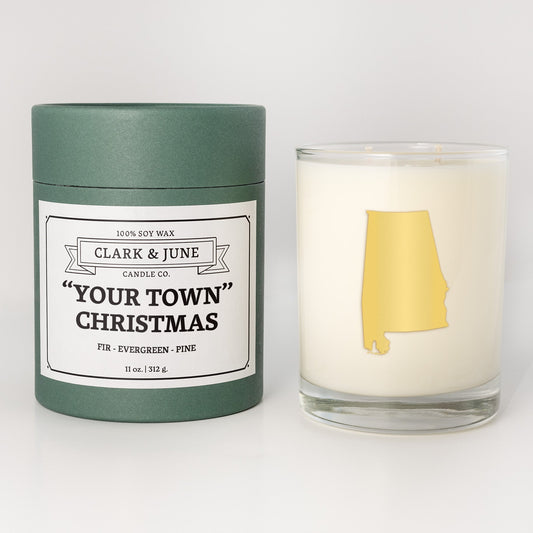 Double wicked soy candle in a 13.5 oz tumbler with the state of   Alabamaprinted in 22k gold foil on the face. Green cylinder packaging with "Your Town" Christmas on the label. SEO Text – Drinking glass, soy wax candle, Christmas Candle, hand poured, small batch, scented candle, Woman Owned, local candle, Housewarming present, gives back, charity, community candle, becomes a cocktail glass, closing gift.