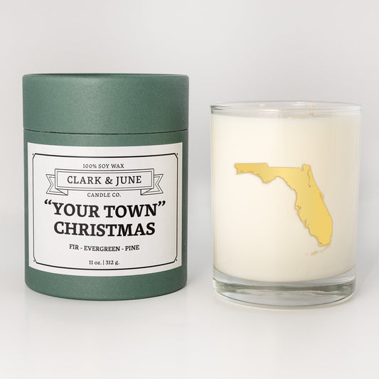 Double wicked soy candle in a 13.5 oz tumbler with the state of Floridaprinted in 22k gold foil on the face. Green cylinder packaging with "Your Town" Christmas on the label. SEO Text – Drinking glass, soy wax candle, Christmas Candle, hand poured, small batch, scented candle, Woman Owned, local candle, Housewarming present, gives back, charity, community candle, becomes a cocktail glass, closing gift.