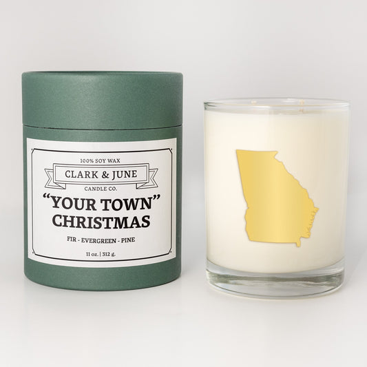 Double wicked soy candle in a 13.5 oz tumbler with the state of   Georgiaprinted in 22k gold foil on the face. Green cylinder packaging with "Your Town" Christmas on the label. SEO Text – Drinking glass, soy wax candle, Christmas Candle, hand poured, small batch, scented candle, Woman Owned, local candle, Housewarming present, gives back, charity, community candle, becomes a cocktail glass, closing gift.