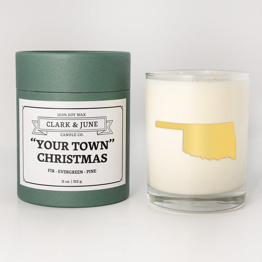 Double wicked soy candle in a 13.5 oz tumbler with the state of Oklahomaprinted in 22k gold foil on the face. Green cylinder packaging with "Your Town" Christmas on the label. SEO Text – Drinking glass, soy wax candle, Christmas Candle, hand poured, small batch, scented candle, Woman Owned, local candle, Housewarming present, gives back, charity, community candle, becomes a cocktail glass, closing gift.