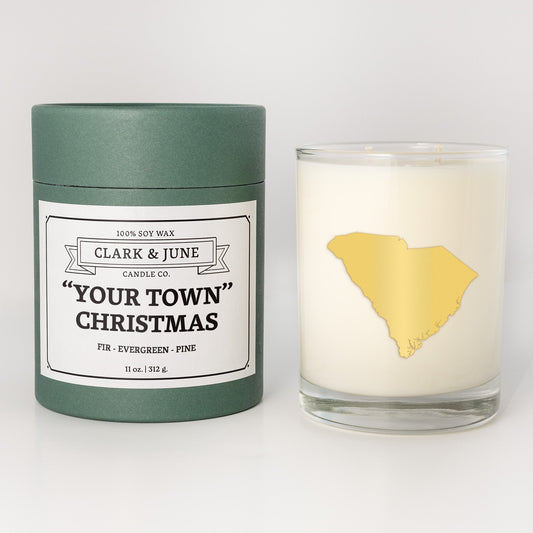 Double wicked soy candle in a 13.5 oz tumbler with the state of South Carolinaprinted in 22k gold foil on the face. Green cylinder packaging with "Your Town" Christmas on the label. SEO Text – Drinking glass, soy wax candle, Christmas Candle, hand poured, small batch, scented candle, Woman Owned, local candle, Housewarming present, gives back, charity, community candle, becomes a cocktail glass, closing gift.