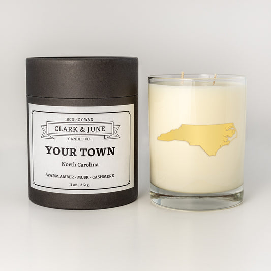 Double wicked soy candle in a 13.5 oz tumbler with the state of North Carolina printed in 22k gold foil on the face. Black cylinder packaging with a customizable label. SEO Text – Drinking glass, soy wax candle, Florida candle, hand poured, small batch, scented candle, Woman Owned, local candle, Housewarming present, gives back, charity, community candle, becomes a cocktail glass, closing gift.