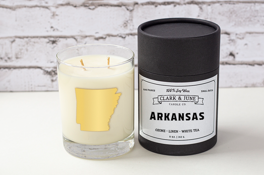 Double wicked soy candle in a 13.5 oz tumbler with the state of Arkansas printed in 22k gold foil on the face. Black cylinder packaging with “Arkansas” on the label. SEO Text – Drinking glass, soy wax candle, Alabama candle, hand poured, small batch, scented candle, Woman Owned, local candle, Housewarming present, gives back, charity, community candle, becomes a cocktail glass, closing gift. 