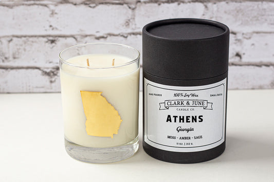 Double wicked soy candle in a 13.5 oz tumbler with the state of Georgia printed in 22k gold foil on the face. Black cylinder packaging with “Athens, Georgia” on the label. SEO Text – Drinking glass, soy wax candle, Alabama candle, hand poured, small batch, scented candle, Woman Owned, local candle, Housewarming present, gives back, charity, community candle, becomes a cocktail glass, closing gift. 