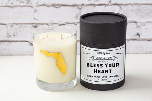 Double wicked soy candle in a 13.5 oz tumbler with the state of Florida printed in 22k gold foil on the face. Black cylinder packaging with “Bless Your Heart” on the label. SEO Text – Drinking glass, soy wax candle, Florida candle, hand poured, small batch, scented candle, Woman Owned, local candle, Housewarming present, gives back, charity, community candle, becomes a cocktail glass, closing gift. 