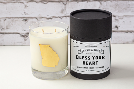Double wicked soy candle in a 13.5 oz tumbler with the state of Georgia printed in 22k gold foil on the face. Black cylinder packaging with “Bless Your Heart” on the label. SEO Text – Drinking glass, soy wax candle, Georgia candle, hand poured, small batch, scented candle, Woman Owned, local candle, Housewarming present, gives back, charity, community candle, becomes a cocktail glass, closing gift. 