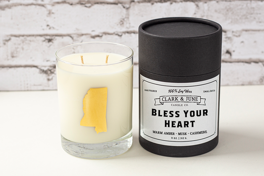 Double wicked soy candle in a 13.5 oz tumbler with the state of Mississippi printed in 22k gold foil on the face. Black cylinder packaging with “Bless Your Heart” on the label. SEO Text – Drinking glass, soy wax candle, Mississippi candle, hand poured, small batch, scented candle, Woman Owned, local candle, Housewarming present, gives back, charity, community candle, becomes a cocktail glass, closing gift. 