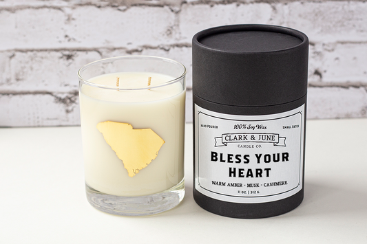 Double wicked soy candle in a 13.5 oz tumbler with the state of South Carolina printed in 22k gold foil on the face. Black cylinder packaging with “Bless Your Heart” on the label. SEO Text – Drinking glass, soy wax candle, South Carolina candle, hand poured, small batch, scented candle, Woman Owned, local candle, Housewarming present, gives back, charity, community candle, becomes a cocktail glass, closing gift.