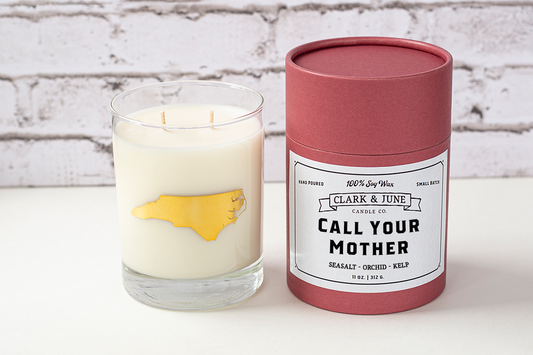 Double wicked soy candle in a 13.5 oz tumbler with the state of North Carolina printed in 22k gold foil on the face. Black cylinder packaging with “Call Your Mother” on the label. SEO Text – Drinking glass, soy wax candle, North Carolina candle, hand poured, small batch, scented candle, Woman Owned, local candle, Housewarming present, gives back, charity, community candle, becomes a cocktail glass, closing gift. Mother's Day Candle, Mothers Day