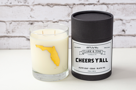 Double wicked soy candle in a 13.5 oz tumbler with the state of Florida printed in 22k gold foil on the face. Black cylinder packaging with “Cheers Y’All” on the label. SEO Text – Drinking glass, soy wax candle, Florida candle, hand poured, small batch, scented candle, Woman Owned, local candle, Housewarming present, gives back, charity, community candle, becomes a cocktail glass, closing gift. 
