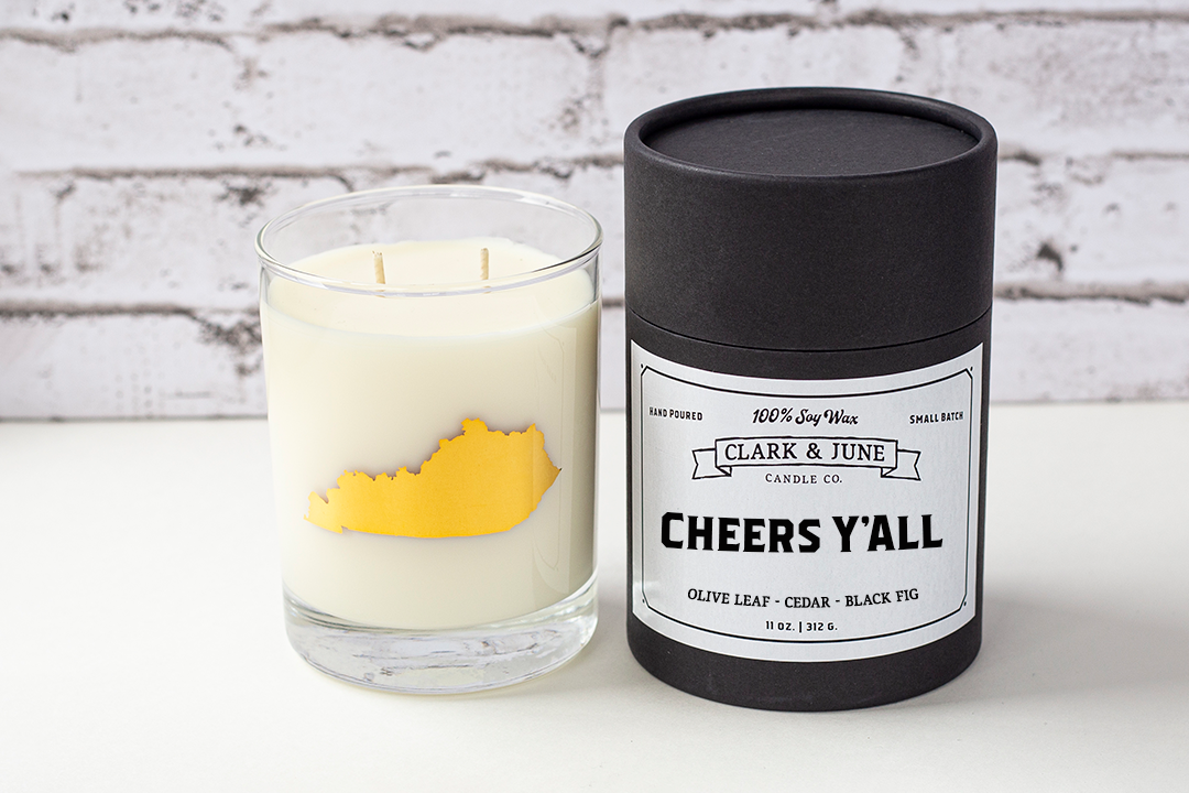Double wicked soy candle in a 13.5 oz tumbler with the state of Kentucky printed in 22k gold foil on the face. Black cylinder packaging with “Cheers Y’All” on the label. SEO Text – Drinking glass, soy wax candle, Kentucky candle, hand poured, small batch, scented candle, Woman Owned, local candle, Housewarming present, gives back, charity, community candle, becomes a cocktail glass, closing gift. 