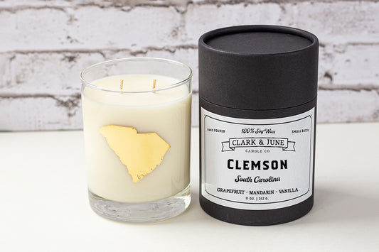 Double wicked soy candle in a 13.5 oz tumbler with the state of South Carolina printed in 22k gold foil on the face. Black cylinder packaging with “Clemson” on the label. SEO Text – Drinking glass, soy wax candle, South Carolina candle, hand poured, small batch, scented candle, Woman Owned, local candle, Housewarming present, gives back, charity, community candle, becomes a cocktail glass, closing gift.