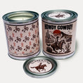 Load image into Gallery viewer, 14oz Cowboy design soy wax candle in a pint sized paint can made by Clark & June Candle Co. The candle is wrapped with a brown and tan label showing cowboys on bucking horses and cacti on the back with a wood cut design of a Cowboy riding on a horse by a cabin with the phrase “Howdy Cowboy” on the front. The scent is Moss – Amber - Sage and was hand poured in small batches. 

Cowboy Candle, Scented Candle, Paint Can Candle. Single Cotton Wick

