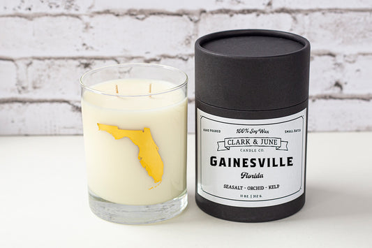 Double wicked soy candle in a 13.5 oz tumbler with the state of Florida printed in 22k gold foil on the face. Black cylinder packaging with “Gainesville” on the label. SEO Text – Drinking glass, soy wax candle, Florida candle, hand poured, small batch, scented candle, Woman Owned, local candle, Housewarming present, gives back, charity, community candle, becomes a cocktail glass, closing gift. 
