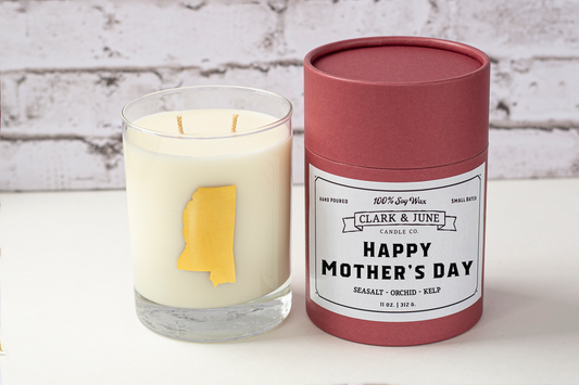 Double wicked soy candle in a 13.5 oz tumbler with the state of Mississippi printed in 22k gold foil on the face. Black cylinder packaging with “Happy Mother’s Day” on the label. SEO Text – Drinking glass, soy wax candle, Mississippi candle, hand poured, small batch, scented candle, Woman Owned, local candle, Housewarming present, gives back, charity, community candle, becomes a cocktail glass, closing gift. 