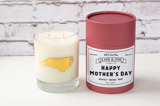 Double wicked soy candle in a 13.5 oz tumbler with the state of North Carolina printed in 22k gold foil on the face. Black cylinder packaging with “Happy Mother’s Day” on the label. SEO Text – Drinking glass, soy wax candle, North Carolina candle, hand poured, small batch, scented candle, Woman Owned, local candle, Housewarming present, gives back, charity, community candle, becomes a cocktail glass, closing gift.