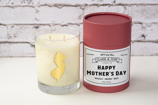 Double wicked soy candle in a 13.5 oz tumbler with the state of New Jersey printed in 22k gold foil on the face. Black cylinder packaging with “Happy Mother’s Day” on the label. SEO Text – Drinking glass, soy wax candle, New Jersey candle, hand poured, small batch, scented candle, Woman Owned, local candle, Housewarming present, gives back, charity, community candle, becomes a cocktail glass, closing gift.