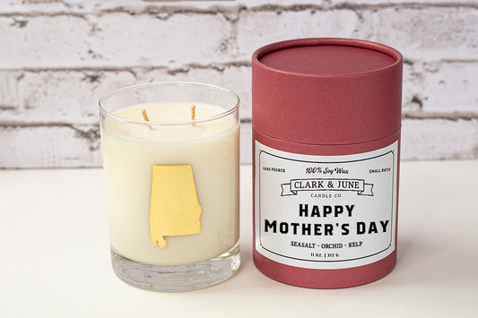 Double wicked soy candle in a 13.5 oz tumbler with the state of Alabama printed in 22k gold foil on the face. Black cylinder packaging with “Happy Mother’s Day” on the label. SEO Text – Drinking glass, soy wax candle, Alabama candle, hand poured, small batch, scented candle, Woman Owned, local candle, Housewarming present, gives back, charity, community candle, becomes a cocktail glass, closing gift. Mother's Day Candle