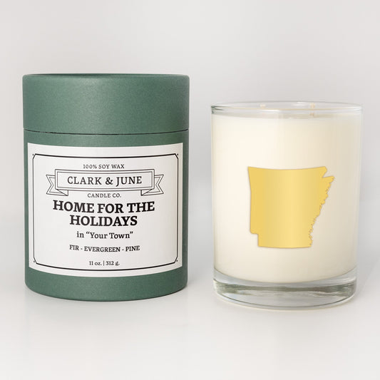 Double wicked soy candle in a 13.5 oz tumbler with the state of Arkansasprinted in 22k gold foil on the face. Green cylinder packaging with Home for the Holidays in "Your Town"on the label. SEO Text – Drinking glass, soy wax candle, Christmas Candle, hand poured, small batch, scented candle, Woman Owned, local candle, Housewarming present, gives back, charity, community candle, becomes a cocktail glass, closing gift. 