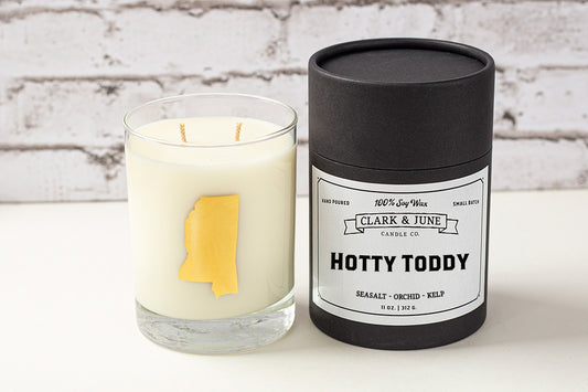 Double wicked soy candle in a 13.5 oz tumbler with the state of Mississippi printed in 22k gold foil on the face. Black cylinder packaging with “Hotty Toddy” on the label. SEO Text – Drinking glass, soy wax candle, Mississippi candle, hand poured, small batch, scented candle, Woman Owned, local candle, Housewarming present, gives back, charity, community candle, becomes a cocktail glass, closing gift. 