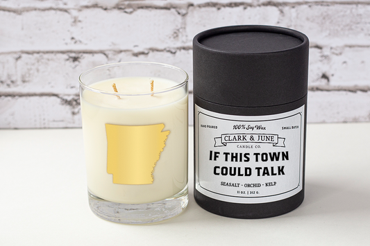Double wicked soy candle in a 13.5 oz tumbler with the state of Arkansas printed in 22k gold foil on the face. Black cylinder packaging with “If This Town Could Talk” on the label. SEO Text – Drinking glass, soy wax candle, Arkansas candle, hand poured, small batch, scented candle, Woman Owned, local candle, Housewarming present, gives back, charity, community candle, becomes a cocktail glass, closing gift. 