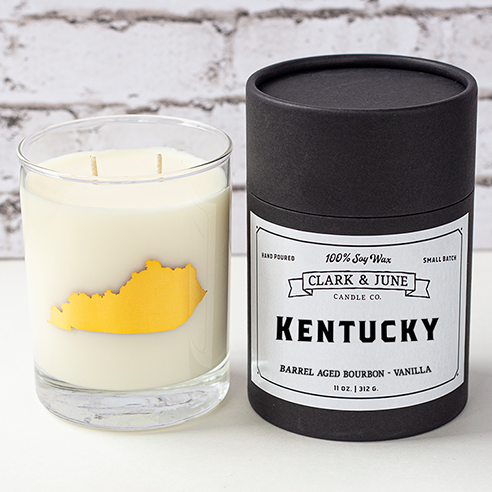Double wicked soy candle in a 13.5 oz tumbler with the state of Kentucky printed in 22k gold foil on the face. Black cylinder packaging with “Kentucky” on the label. 