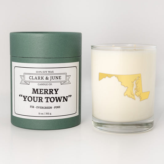 Double wicked soy candle in a 13.5 oz tumbler with the state of Marylandprinted in 22k gold foil on the face. Green cylinder packaging with Merry "Your Town" on the label. SEO Text – Drinking glass, soy wax candle, Christmas Candle, hand poured, small batch, scented candle, Woman Owned, local candle, Housewarming present, gives back, charity, community candle, becomes a cocktail glass, closing gift. 