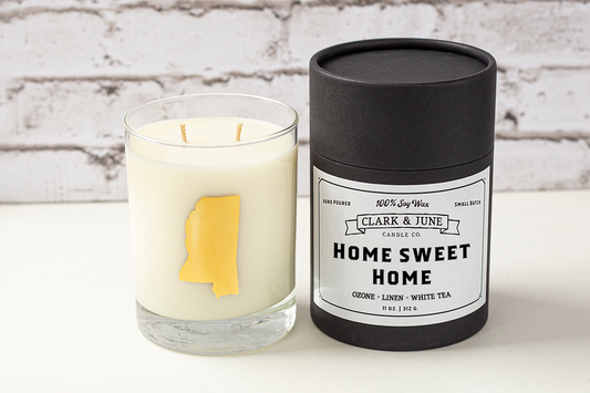Double wicked soy candle in a 13.5 oz tumbler with the state of Mississippi printed in 22k gold foil on the face. Black cylinder packaging with “Home Sweet Home” on the label. SEO Text – Drinking glass, soy wax candle, Mississippi candle, hand poured, small batch, scented candle, Woman Owned, local candle, Housewarming present, gives back, charity, community candle, becomes a cocktail glass, closing gift. 